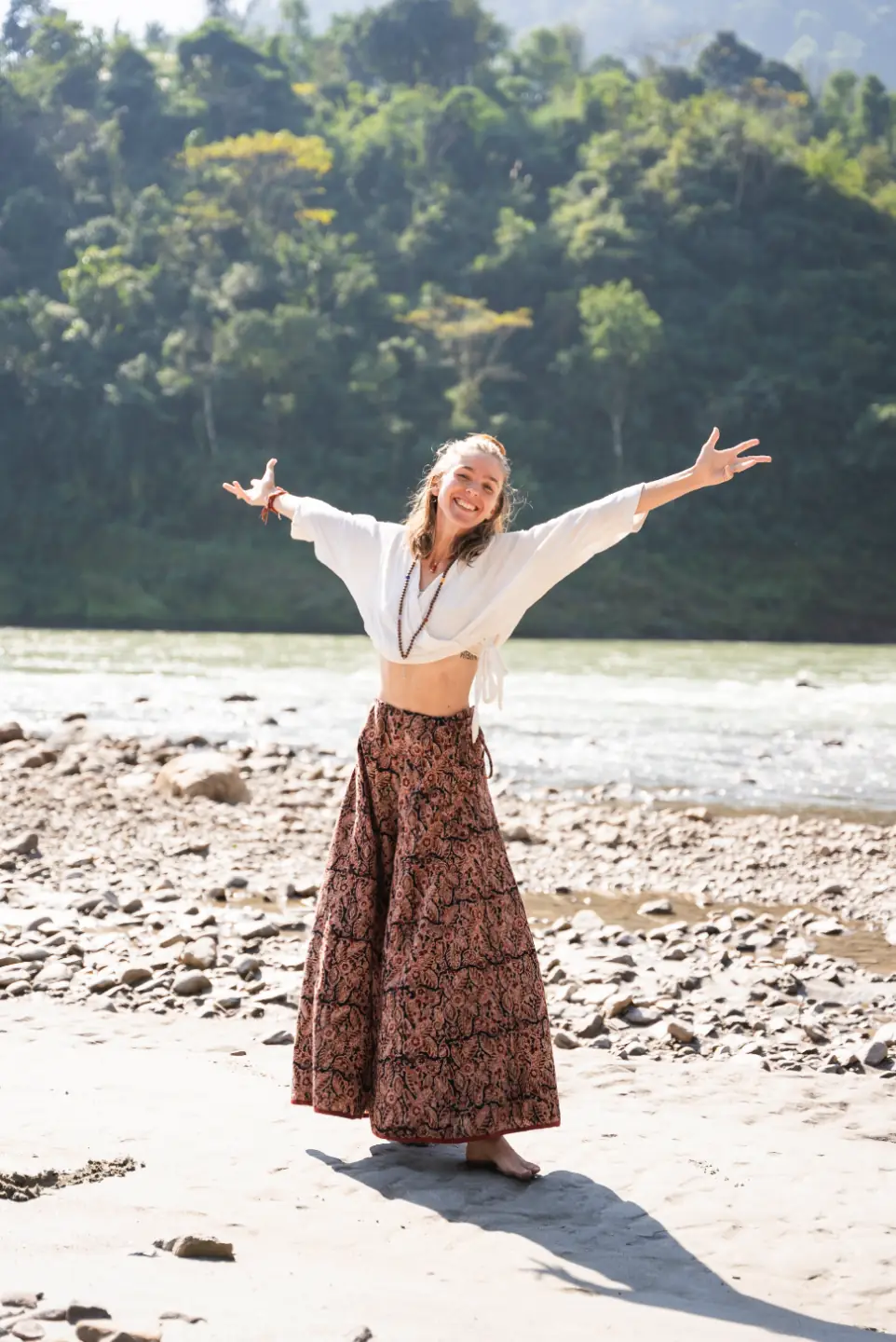 Paige with arms open wide on the banks of the Ganges in Rishikesh