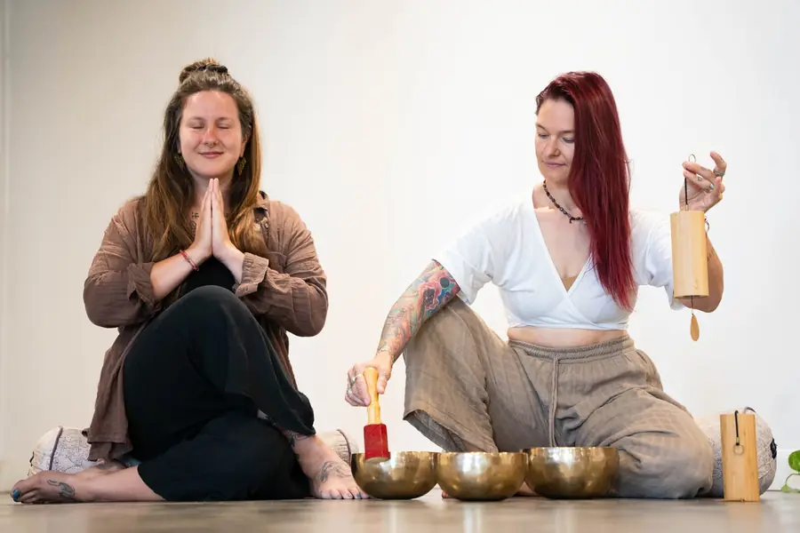 Two teachers with hands in prayer beside singing bowls