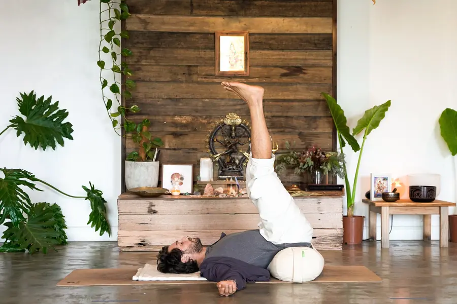 A student holding a supported shoulder stand by the studio altar