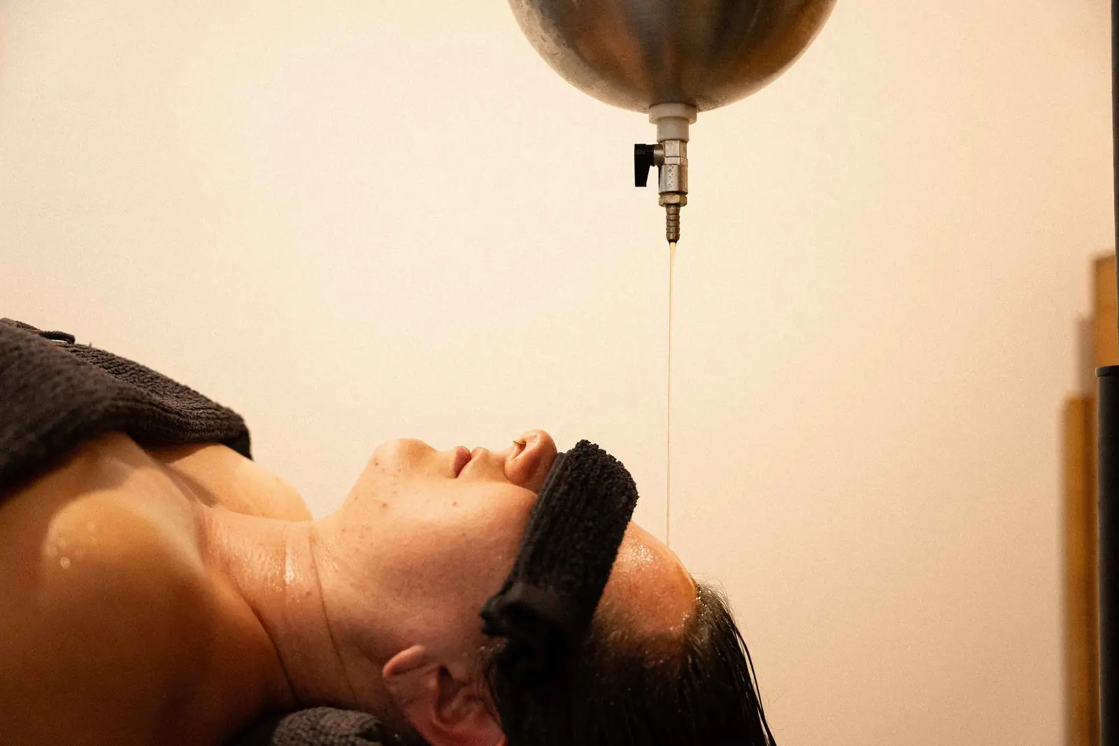 Warm oil streaming onto the forehead during a Shirodhara treatment